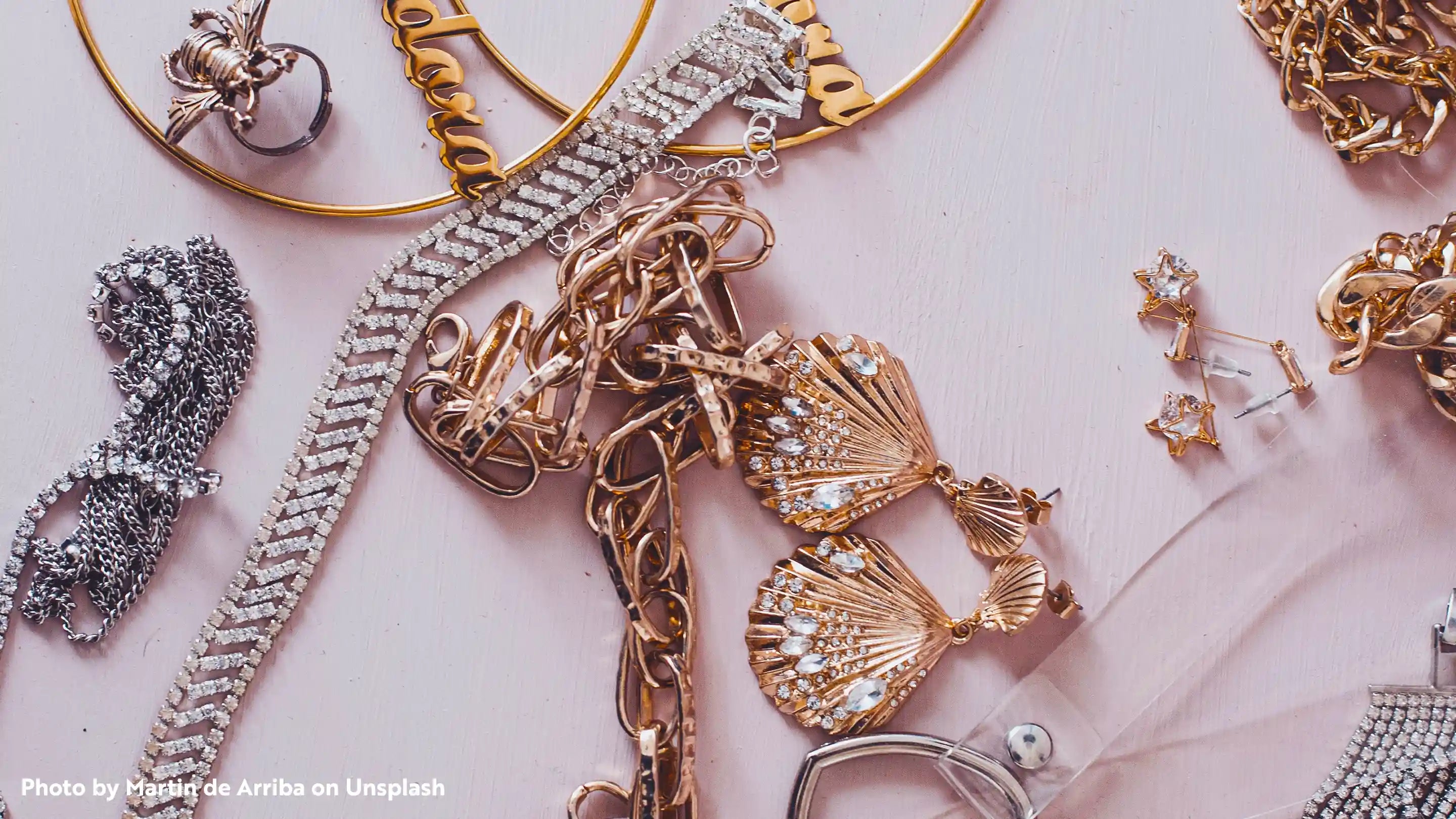 Different types of gold and silver jewelry on a pink background