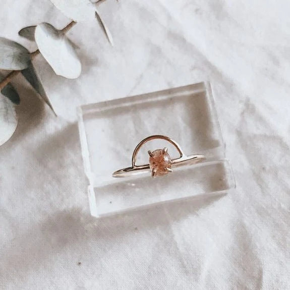 A ring with a pink gem. It's sitting on a clear plastic ring stand on cloth.