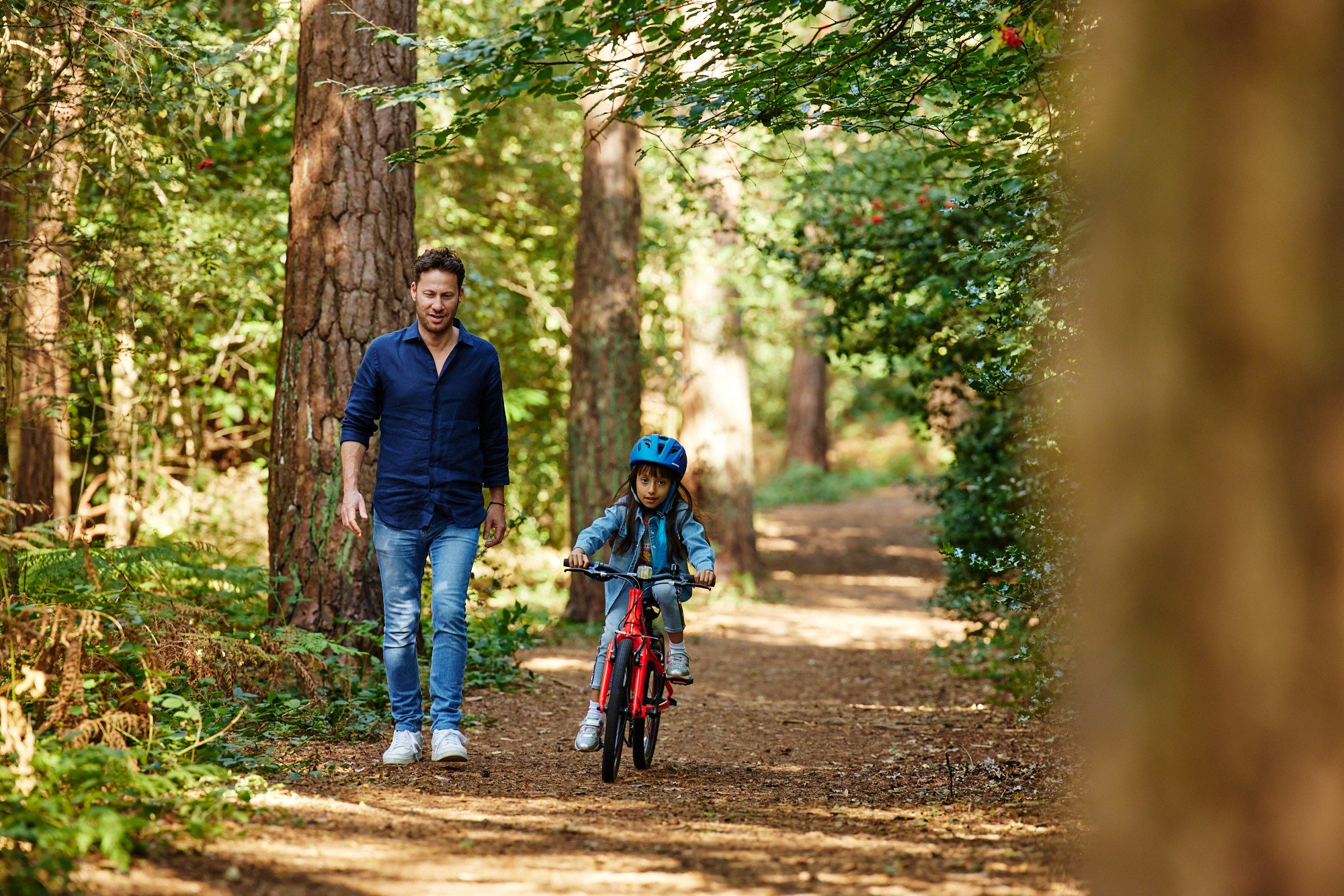a dad standing walking next to his daughter as she rides her bike