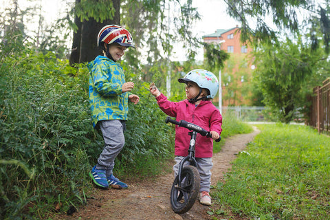 Two kids in the outdoors sitting on a Strider bike