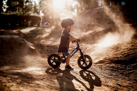 A child sitting on a Strider balance bike at a BMX track