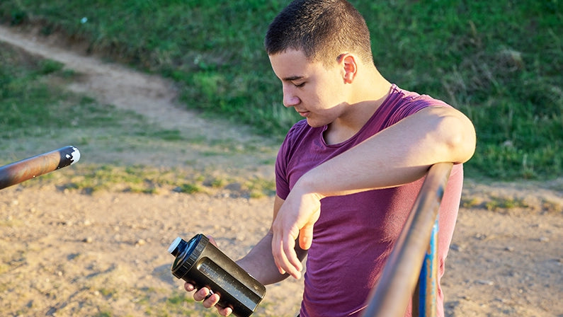 Young man checks his pre workout drink in the black bottle.