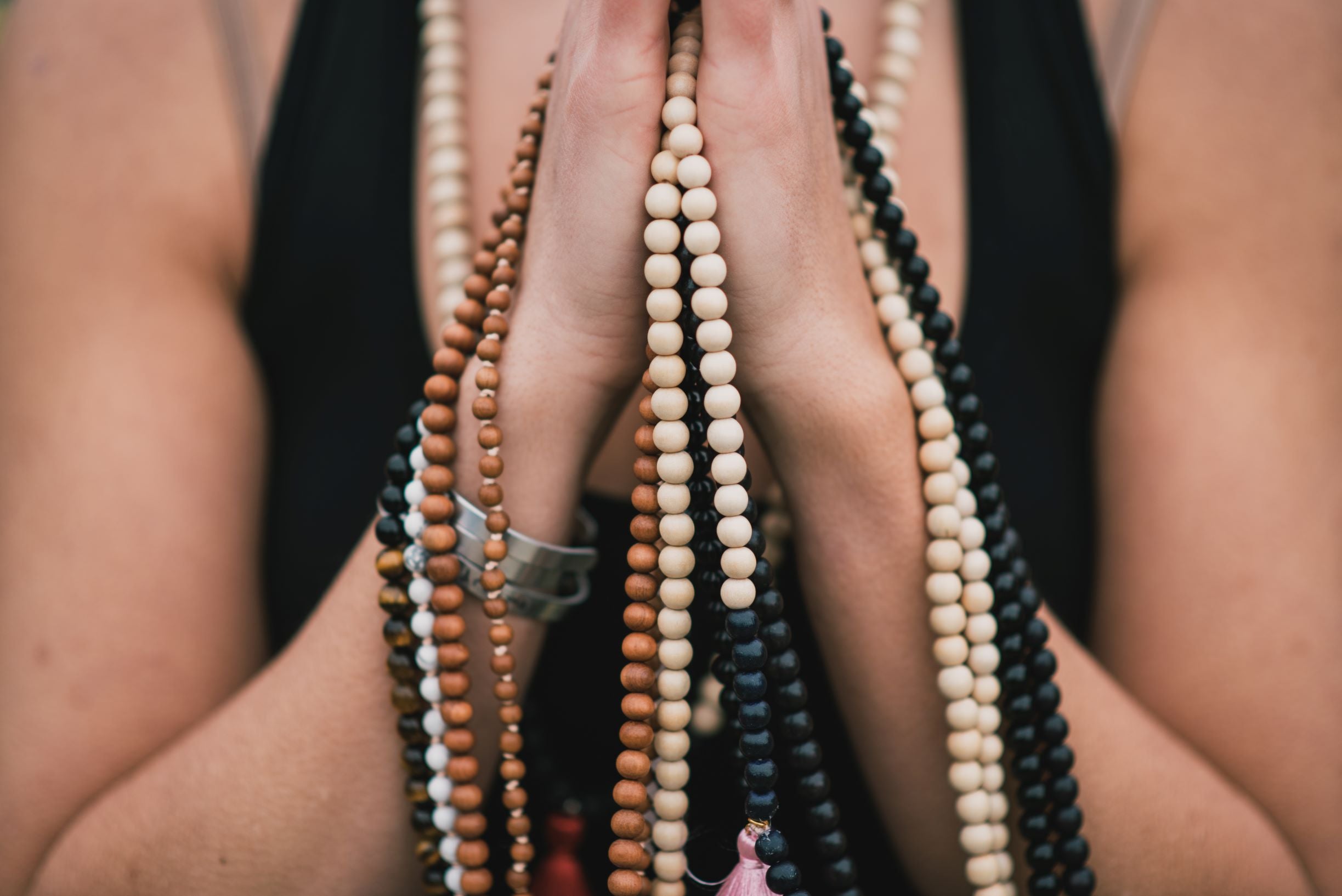 Hands held in prayer while holding handmade mala necklaces, meditating to cleanse the crystals.