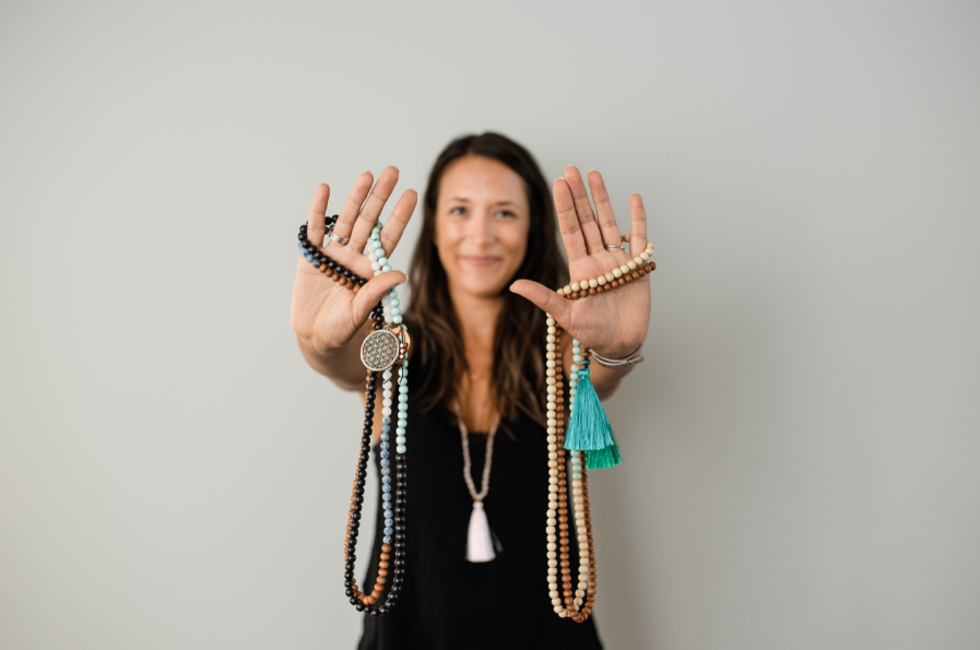 Alysia Waters from Seed + Bloom Designs holding up handmade malas which can be used to connect with affirmations.