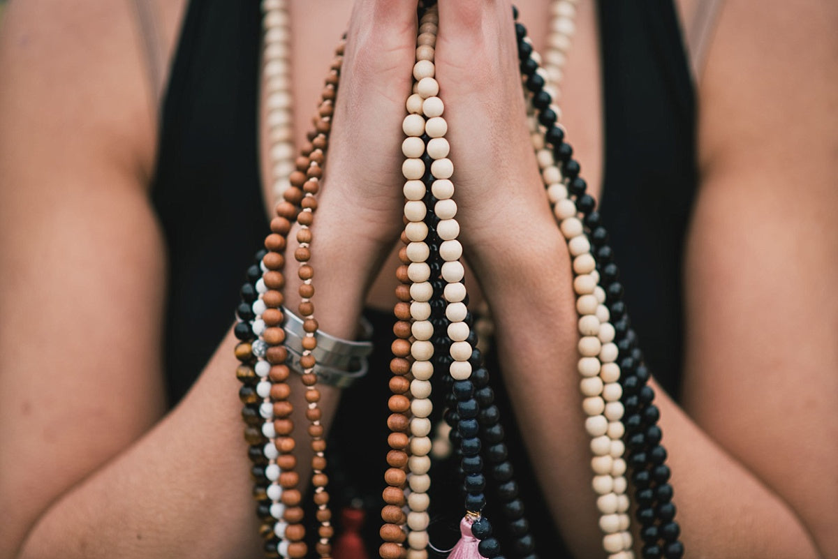 Hands held in prayer position are drapped in multiple handmade malas, made with ethically-sourced mala beads.