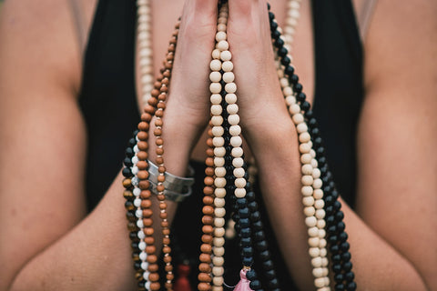 Hands in prayer position holding a collection of handmade malas using crystals for anxiety relief.
