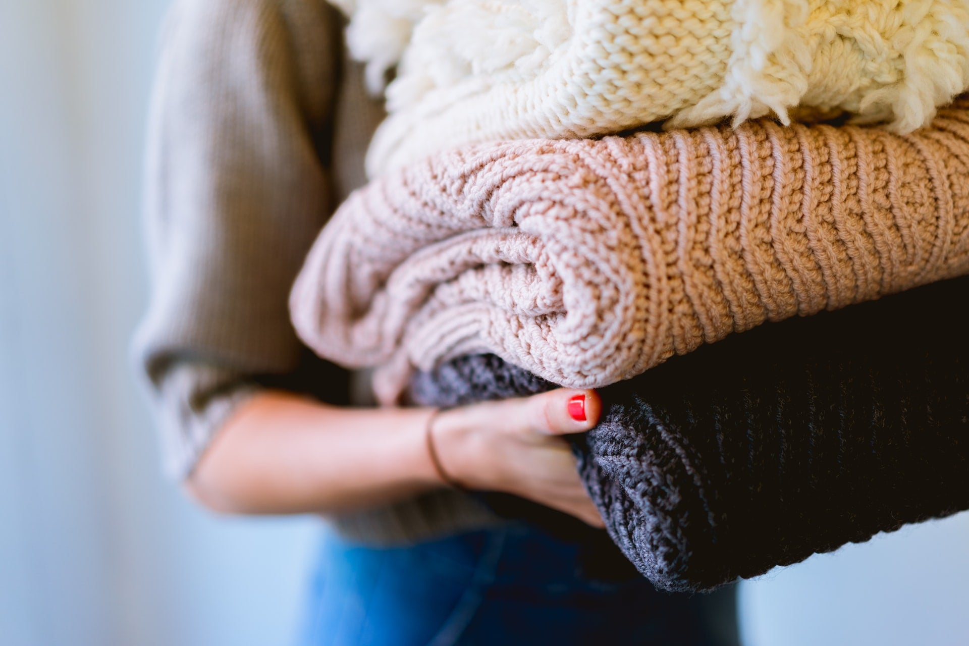 A woman carrying knit sweaters, doing laundry as chores are one of the nicest gifts for people with anxiety.