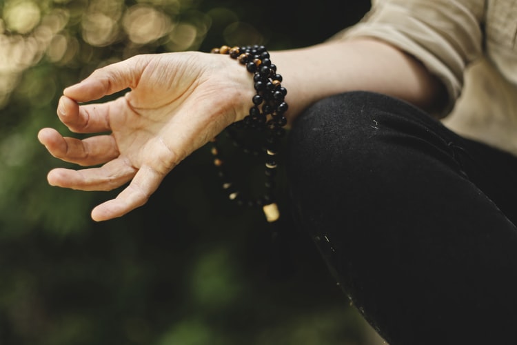 A hand in a meditation position, with the thumb and pointer finger touching, while wearing a black mala bracelet.