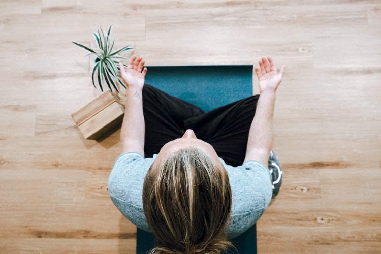 A woman sitting in a meditation pose on her yoga mat, practicing mindfulness at home.