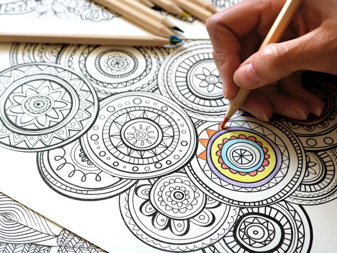 A mindful colouring page being filled in by a hand holding an orange pencil.