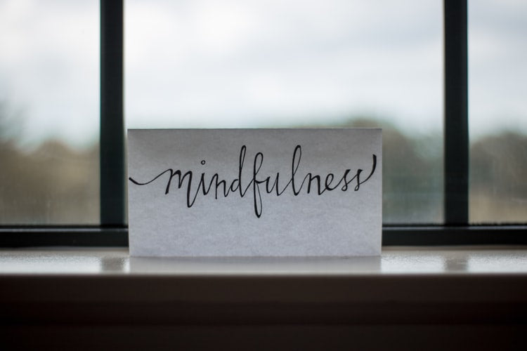 The word 'mindfulness' written on a piece of paper sitting on a ledge in front of a window.