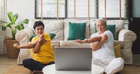 2 seniors exercising at home while watching a computer for virtual workout