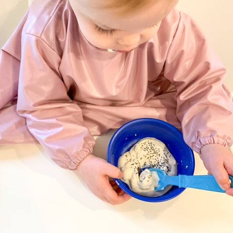 baby eating food independently in a mess me not smock