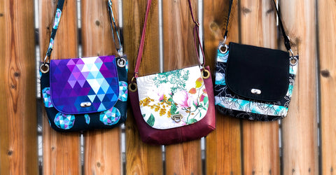 Multiple Jesse Crossbody bags hanging on a fence.