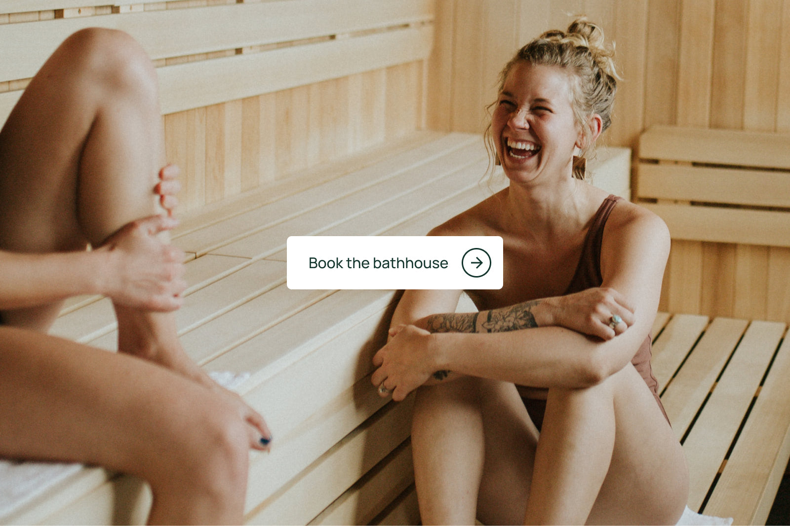 Woman sitting next to a friend in the sauna and laughing