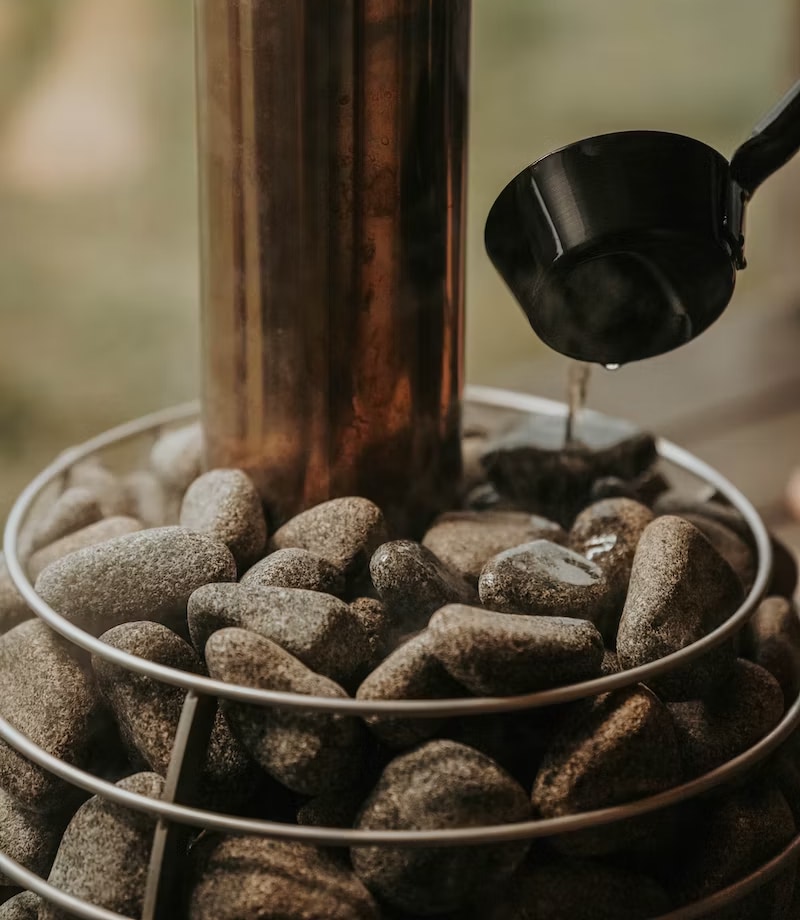 Pouring water over sauna rocks to create steam