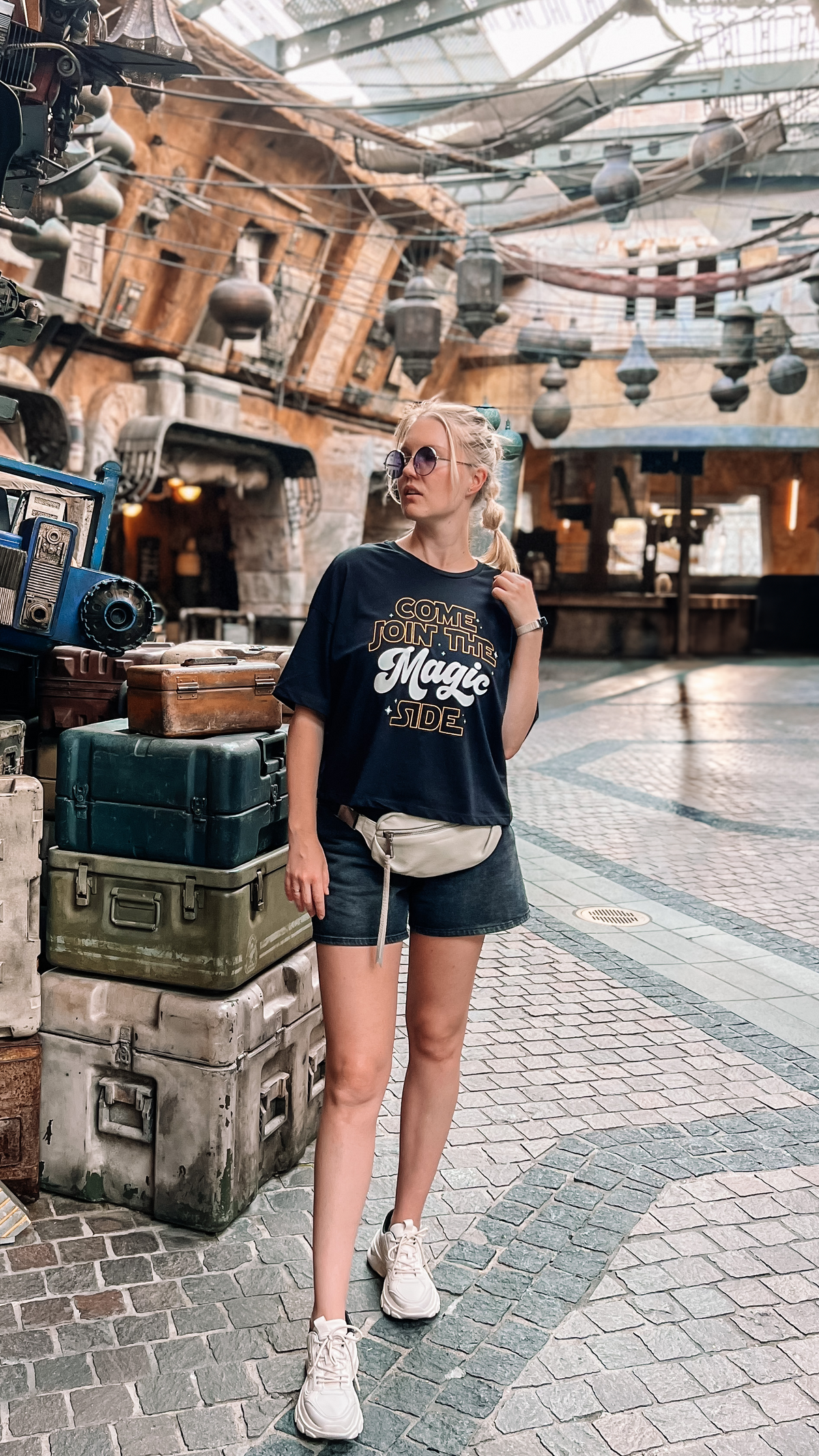 A young woman wearing a "Come Join the Magic Side" crop top stands in front of the Star Wars Trading Post at Disney World.