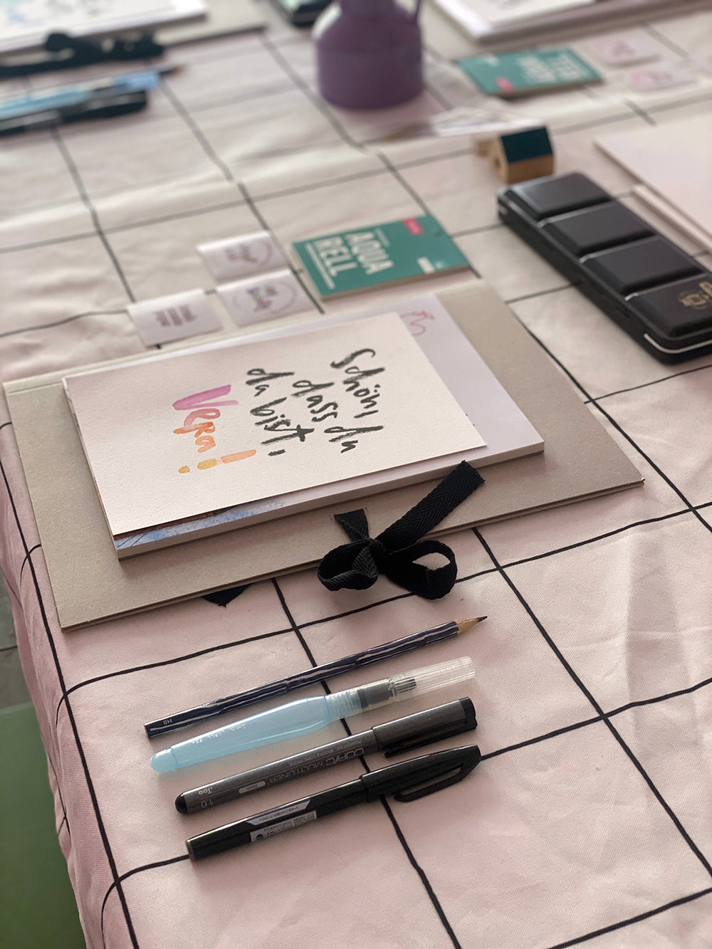 brushmeetspaper - Lettering Workshop, gedeckter Tisch mit Stiften, Willkommens-Karte, karierte Tischdecke 