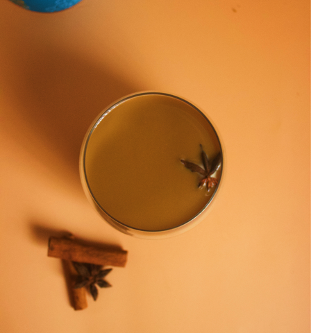 Image shows a cup of Chai, where said image was taken from above. There are sticks of cinnamon on the bottom left