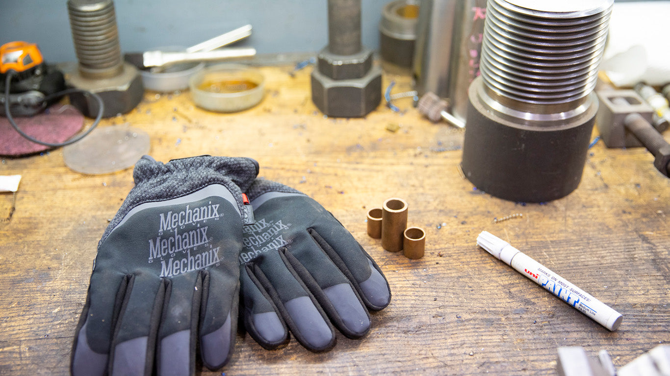 Mechanix Wear ColdWork FastFit gloves laid on a workbench among tools, embodying rugged utility for maintenance tasks.