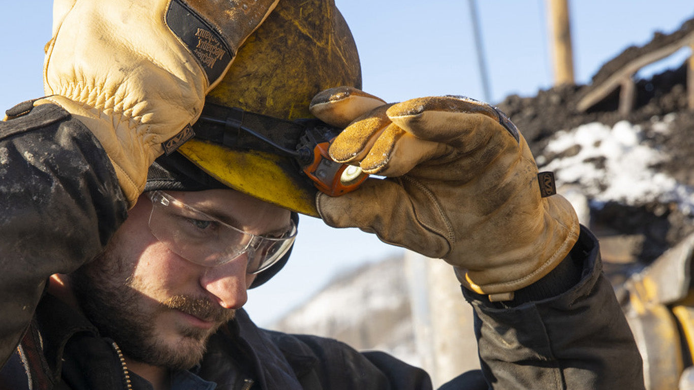 Close-up of a man's hands wearing Mechanix Wear Leather Insulated Driver Gloves, demonstrating their use in adjusting safety equipment on site.