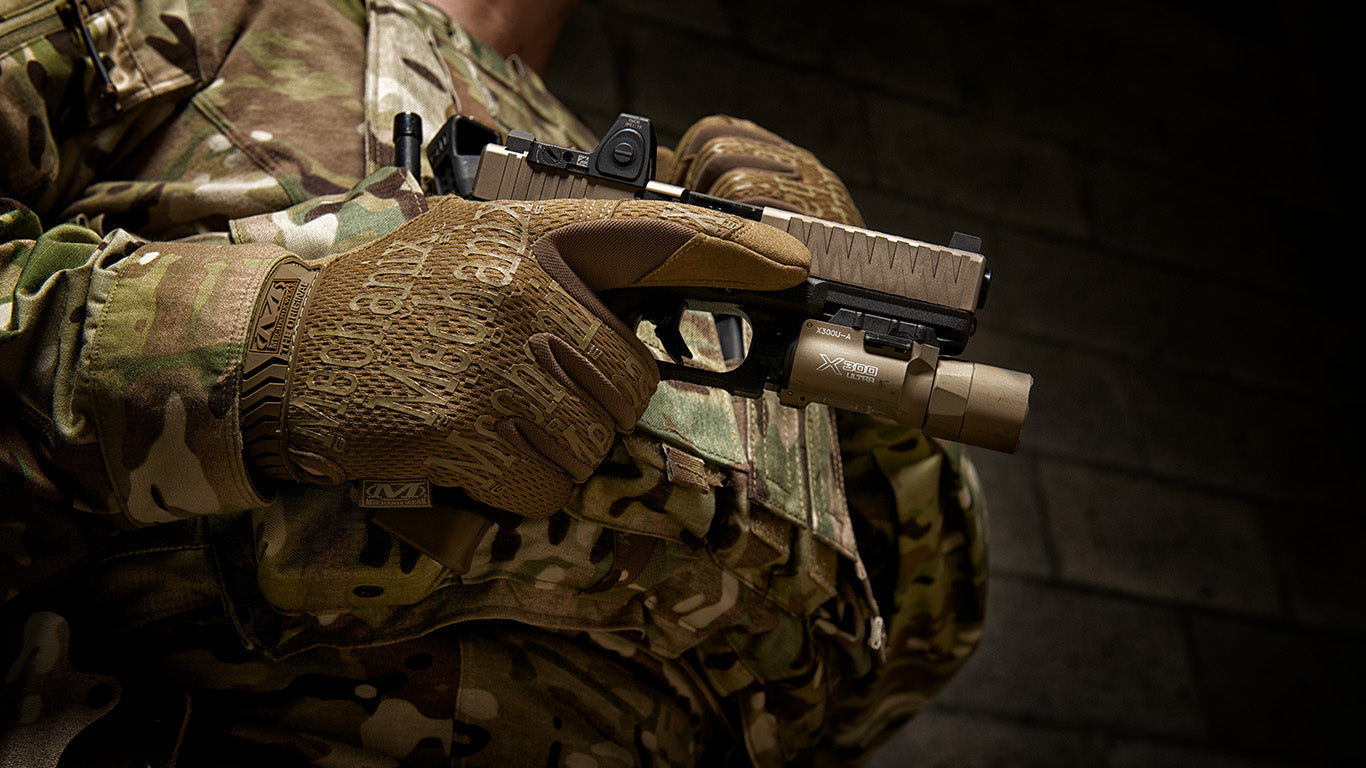 An equipped soldier holding a firearm with Mechanix Wear The Original Coyote Tactical Gloves, showing off the gloves' functional design and grip.