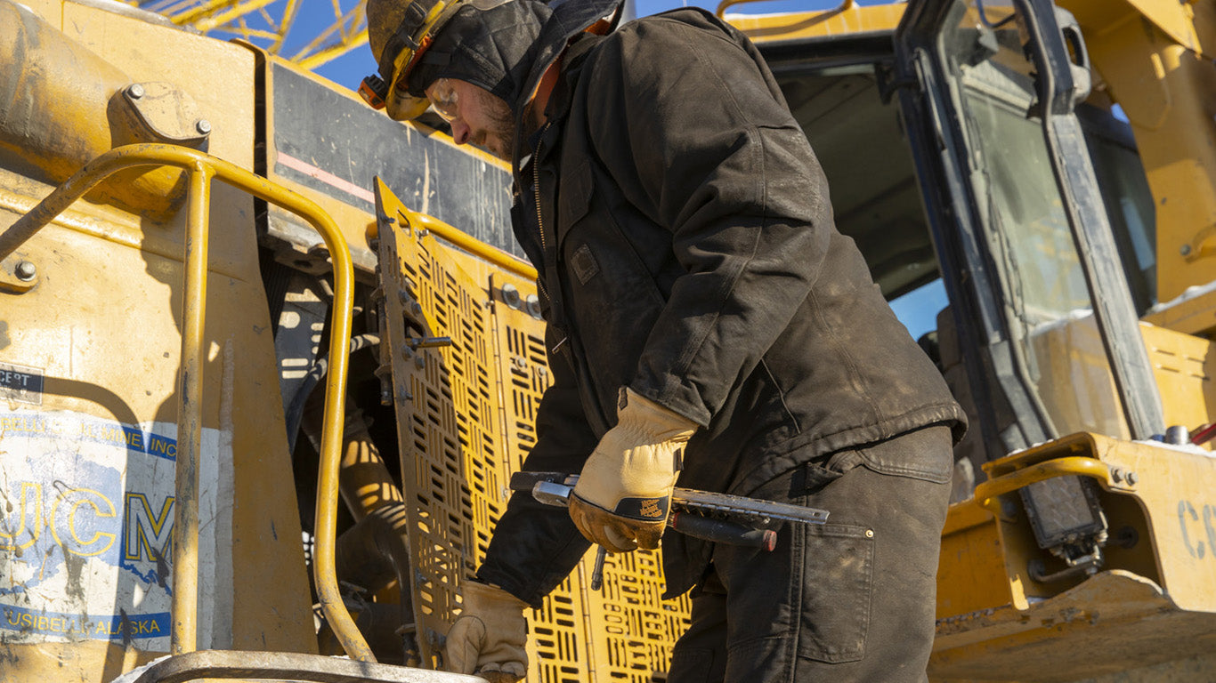 Close-up of a man's hands wearing Mechanix Wear Leather Insulated Driver Gloves, demonstrating their use in adjusting safety equipment on site.