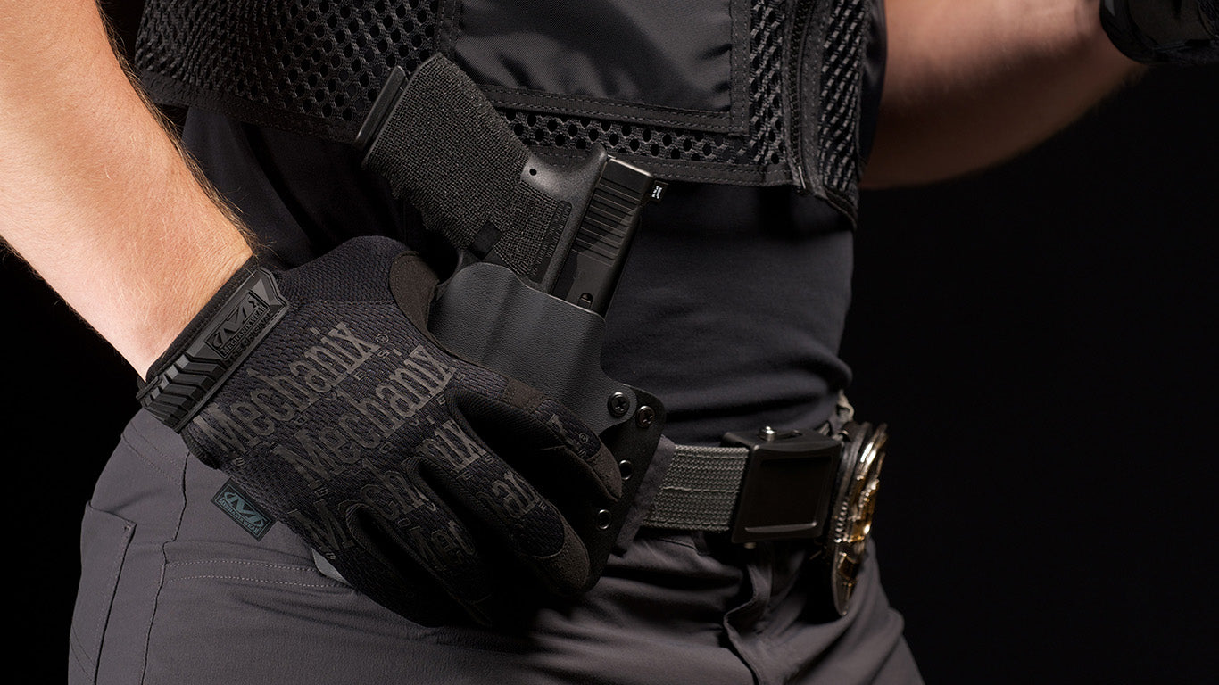 Close-up of a law enforcement officer's hands wearing Mechanix Wear The Original Covert Tactical Gloves while securely handling a service pistol.