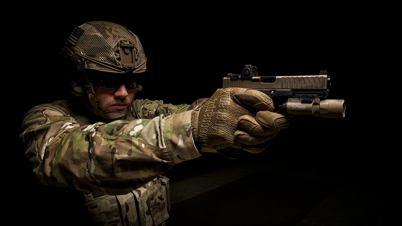 Soldier in full gear aiming a pistol equipped with a tactical light, wearing Mechanix Wear The Original Coyote Tactical Gloves, demonstrating control and precision.