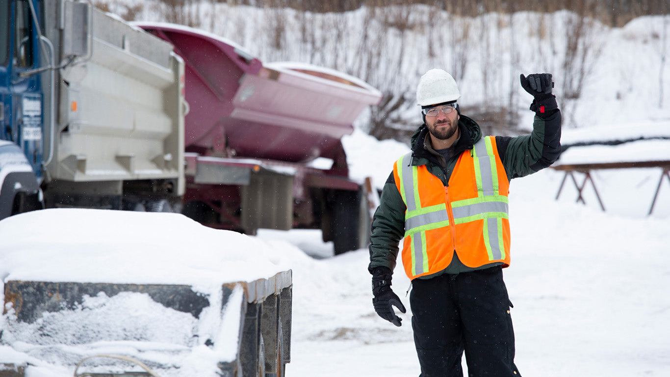 Worker in a hi-vis vest and helmet uses Mechanix ColdWork gloves outdoors in snowy conditions.