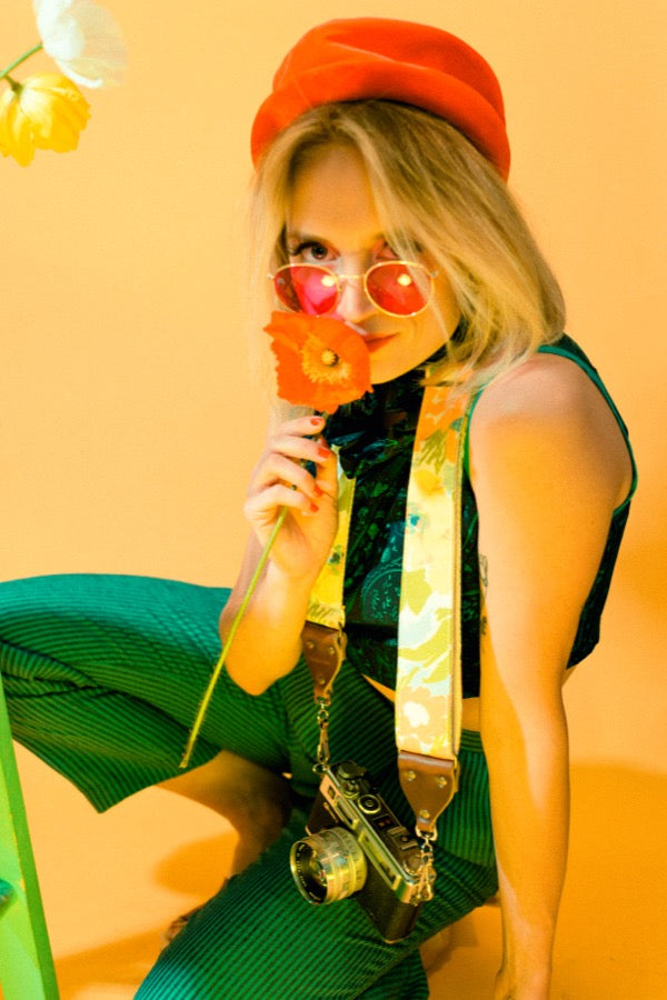 Girl smelling poppy with vintage floral camera strap in mod photoshoot.