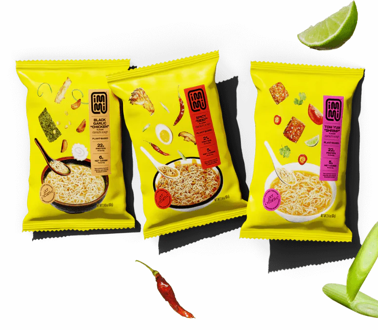 Three colorful instant noodle packets on a black background with various scattered ingredients.