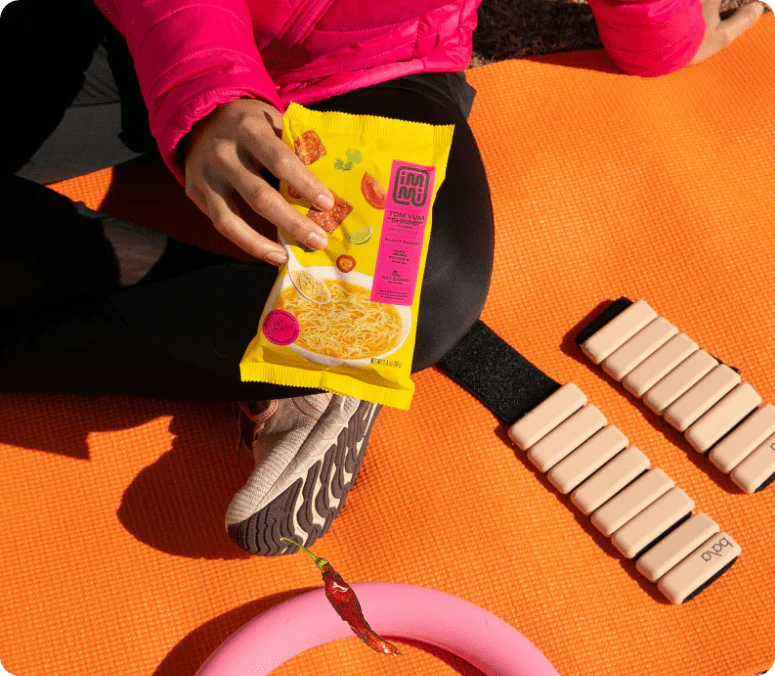 Person holding noodle package on orange mat with exercise equipment.