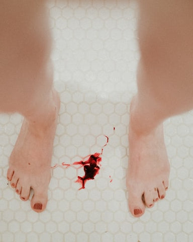 A woman standing in the bathroom with blood on the tile 