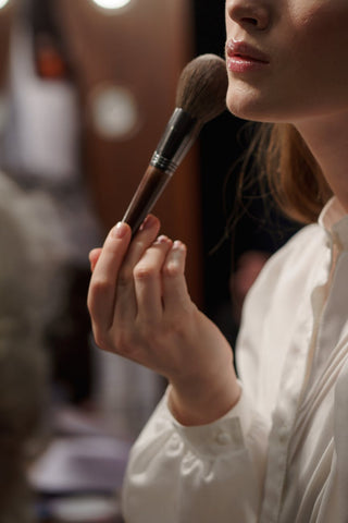 A woman wearing a white top holding a makeup brush 