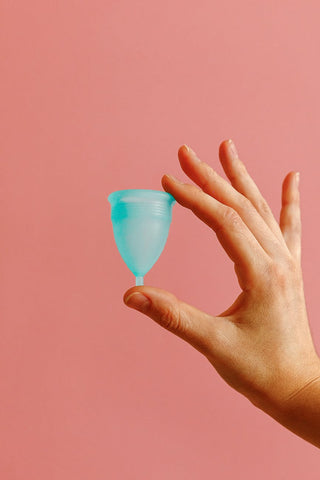 A hand holding a blue menstrual cup 