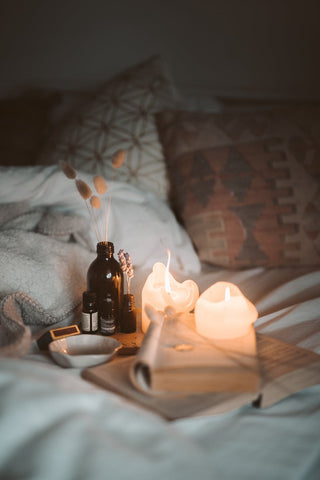 Nicely arranged bed with two lit candles, a book and a dark bottle 