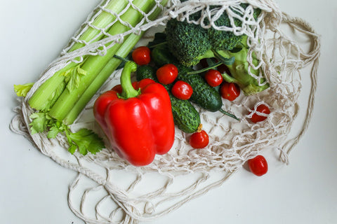 A white netted bag with leeks, bell pepper and some cherry tomatoes