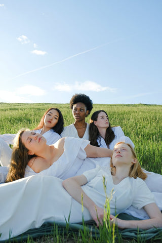A group of varied women in white dresses sitting on the ground 