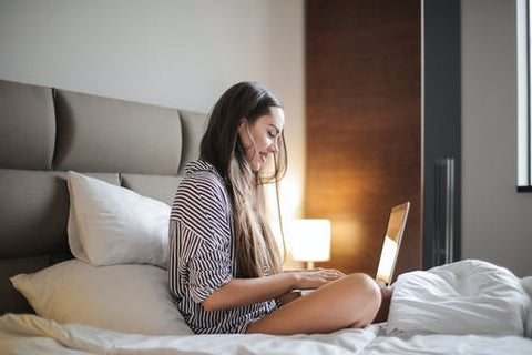 A woman in her night pajamas on a bed working on her laptop