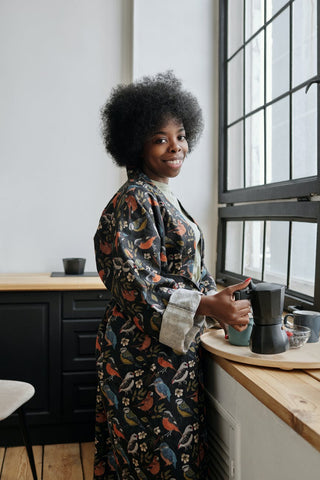 A smiling woman dressed in a night suit holding a kettle 