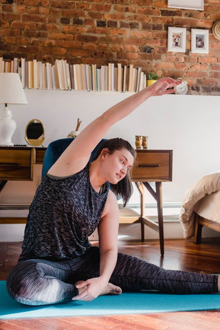 A woman sitting on a Yoga mat stretching her arms 