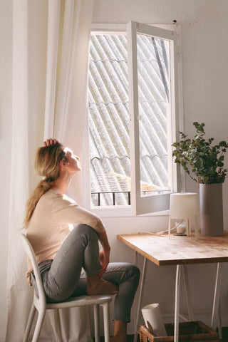 A woman sitting on a chair looking outside a window 