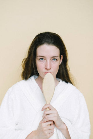 Woman in a white robe holding a hair brush 