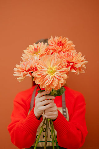Woman holding a bunch of orange flowers covering her face 