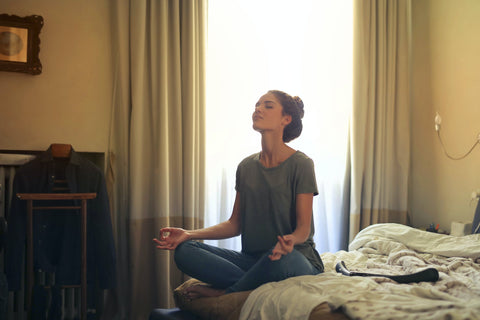 A woman sitting in a yoga posture on her bed 