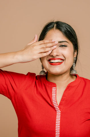Woman in a red kurti placing one hand on her right eye 