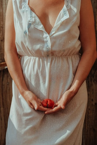 A woman wearing a white dress holding a red fruit 
