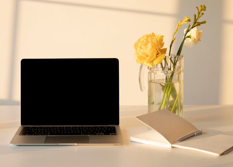 Aesthetic styled desk holding a black laptop, yellow tulips and a journal.