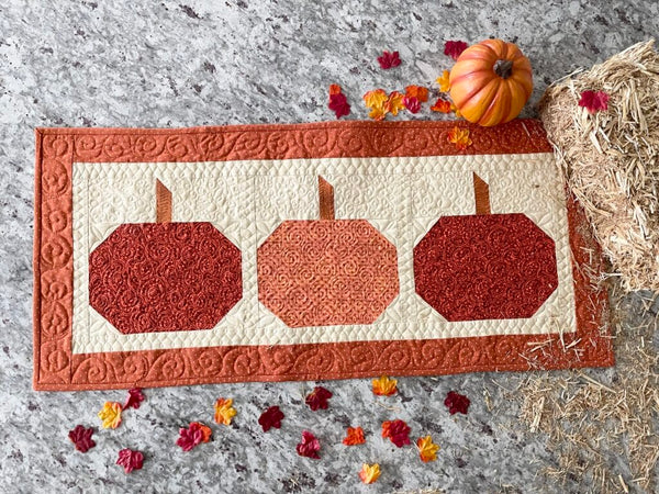 A quilted pumpkin table runner in dark and light shades of orange and cream